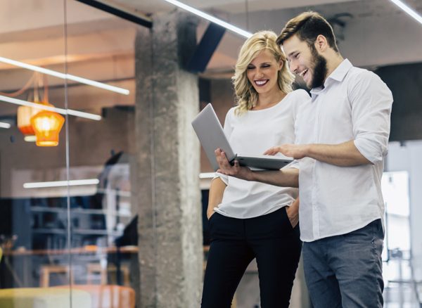 Man showing female co-worker the company travel policy on laptop screen while standing in office