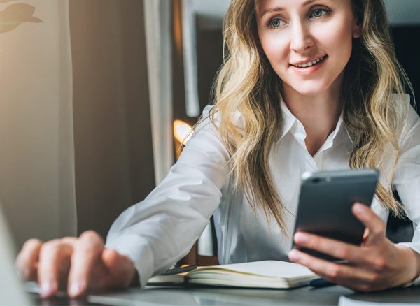 Woman working on laptop while holding cell phone