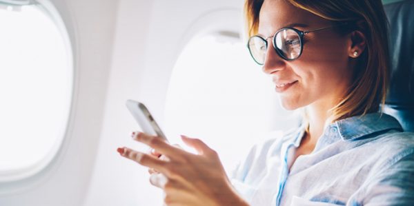 Woman on airplane using business travel technology on her phone