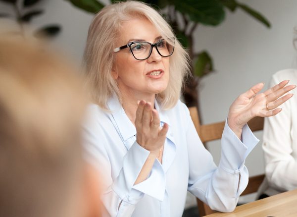 Mature female Travel Manager in glasses speaking at a meeting